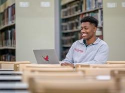 Student in library using laptop with redhawk sticker on it